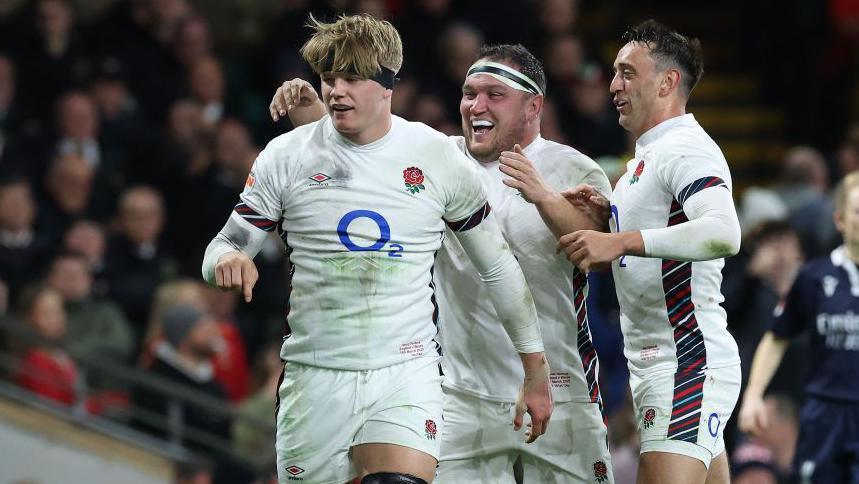 Henry Pollock (left) of England celebrates with team-mates Jamie George and Alex Mitchell after scoring his first try on his international debut