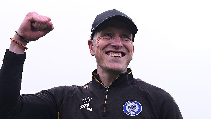 Rochdale boss Jimmy McNulty smiling while clenching his right hand up into a fist after his side's victory against Scunthorpe.