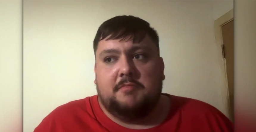 A man in his mid-20s with short brown hair and a short beard. He is wearing a red T-shirt.