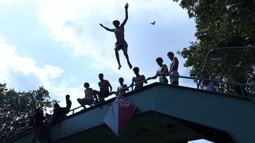 A person jumps off a bridge into the Canal Saint-Martin as public swimming having been allowed earlier on part of it due to rising of temperatures