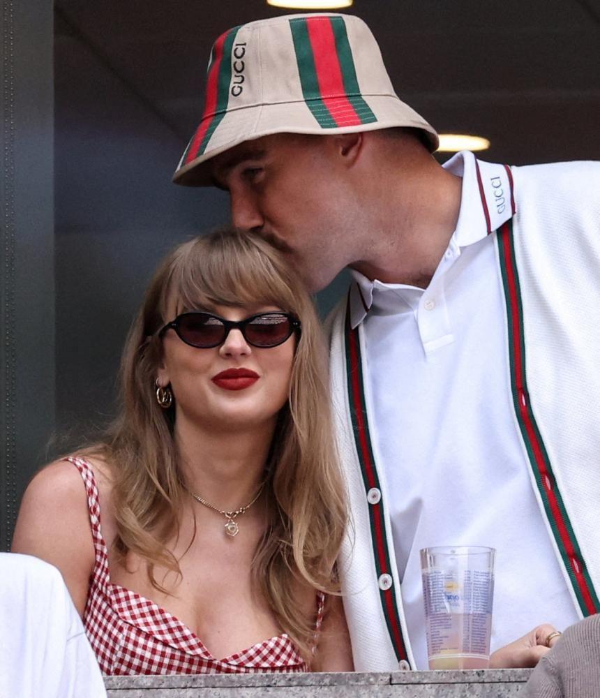 Man kisses the top of woman's head as she sits down