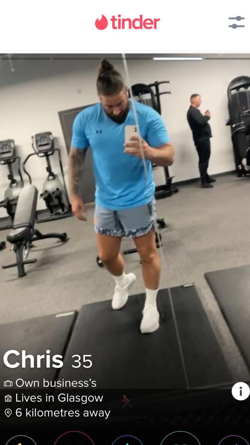 A Tinder dating profile screenshot which shows Harkins on a treadmill in a gym. The photo is a mirror selfie which shows Harkins holding his phone as he runs on the treadmill wearing cut-off denim shorts and light blue t-shirt. He wears white socks and trainers. He has a sleeve tattoo on his right arm. 