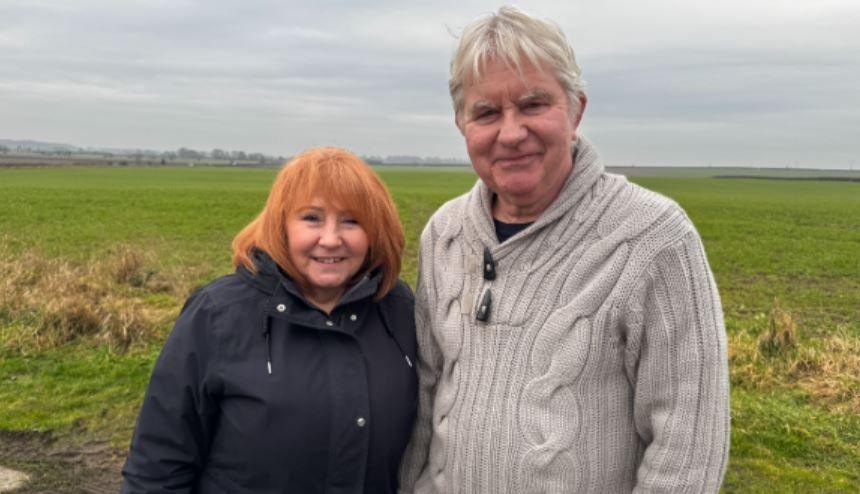 Deborah and Shaun Coleman standing in a field. Mrs Coleman has red-coloured hair and is wearing a dark-coloured winter coat. Mr Coleman has grey hair and is wearing a beige jumper.