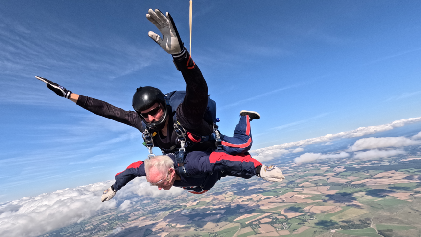 Danny Gibbon during a tandem parachute jump strapped beneath a professional with land and clouds below them