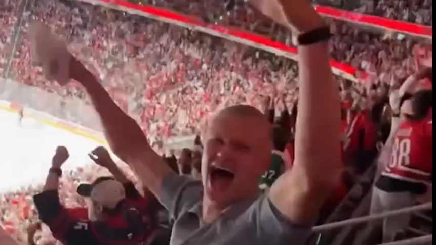 Haaland, wearing a grey polo shirt, celebrating with his arms in the air