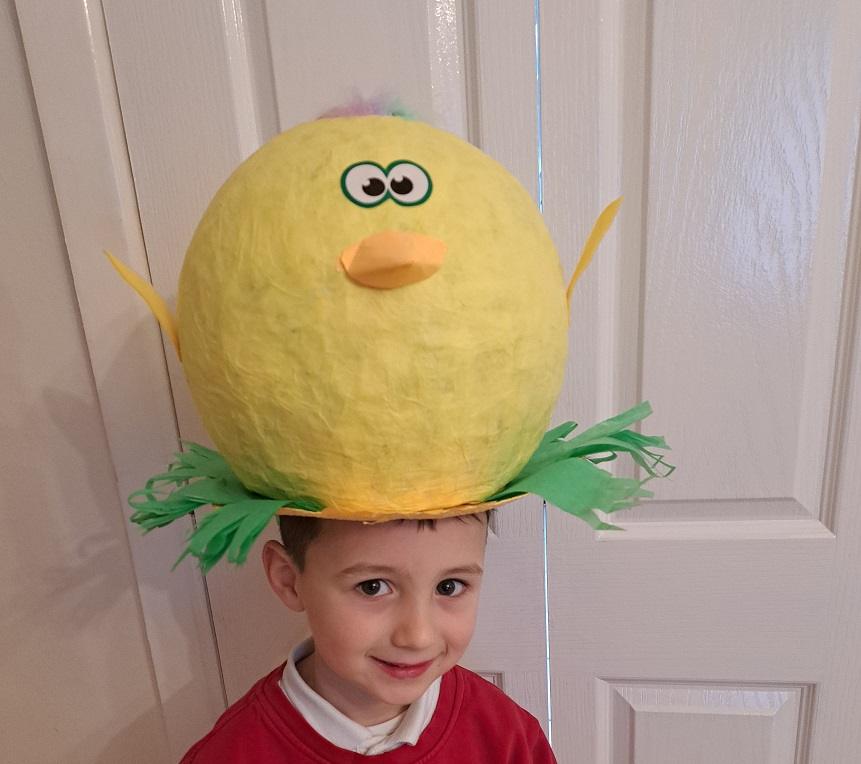 Boy wearing papier-mâché chick hat.