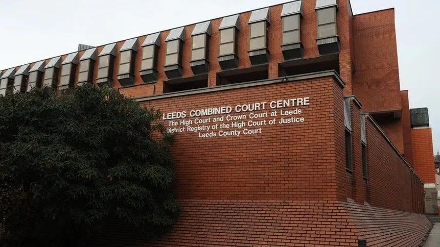 The exterior of Leeds Crown Court - a red brick building with white letters and a tree alongside it.   