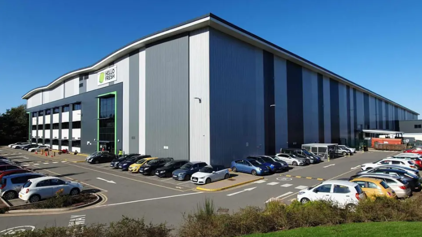 A HelloFresh warehouse made of silver and grey coloured panelling with a car park in front