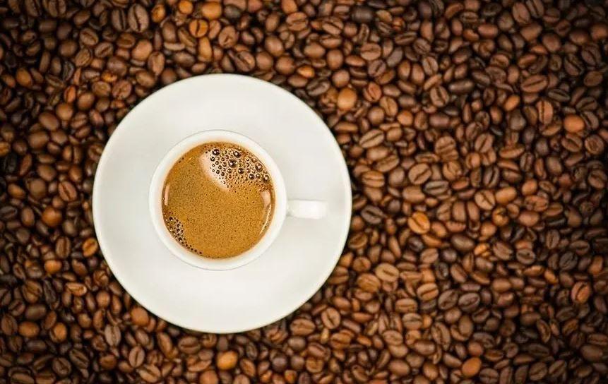 A cup of coffee sitting on top of a layer of coffee beans 