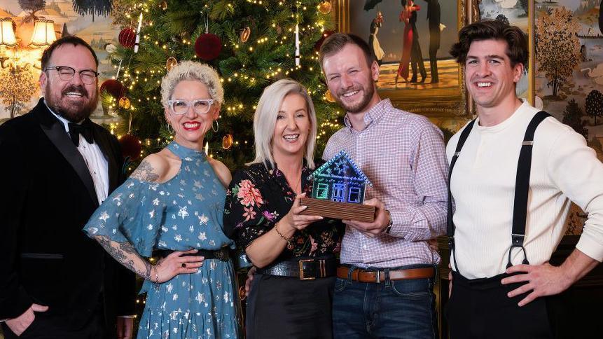 The judges and the homeowners standing in front of a Christmas tree.