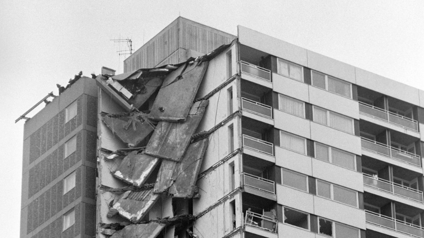 A black and white image showing several collapsed floors on the corner of the Ronan Point building. The two sides, floors and ceilings have fallen, with some concrete panels still hanging off the remaining structure