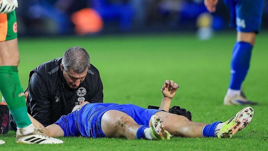 Harry Leonard, lying on the ground, is treated by a member of Peterborough United's medical staff