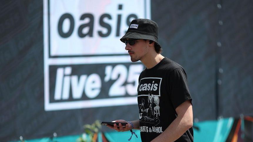 An Oasis fan walks past advertising boards ahead of the first gig of the Oasis Live 25 tour in Cardiff.