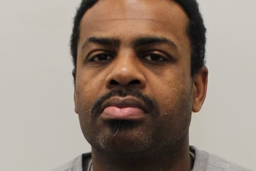 Mug shot of Apapale Adoum who is wearing a grey top and standing against a grey background. He has short black hair and a moustache 