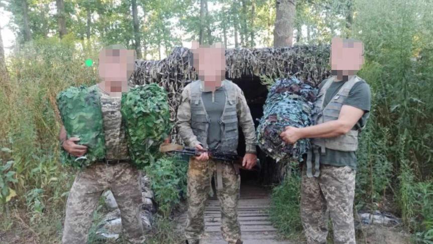 Three soldiers in camouflage holding nets and guns.