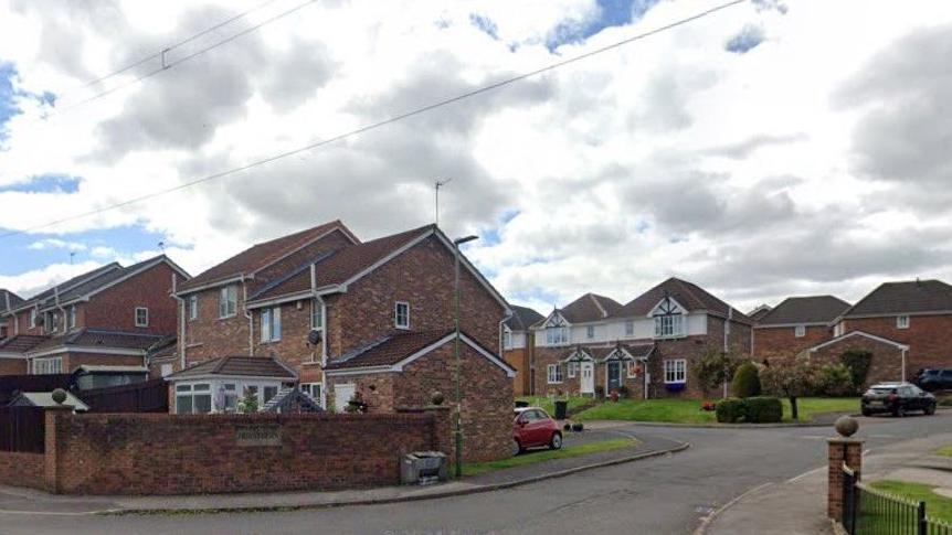 A row of brown-bricked semi-detached houses behind a brick fence in the village.