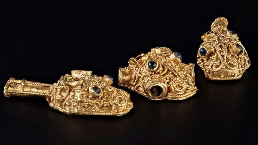 Three gold filigree objects displayed on a black background.