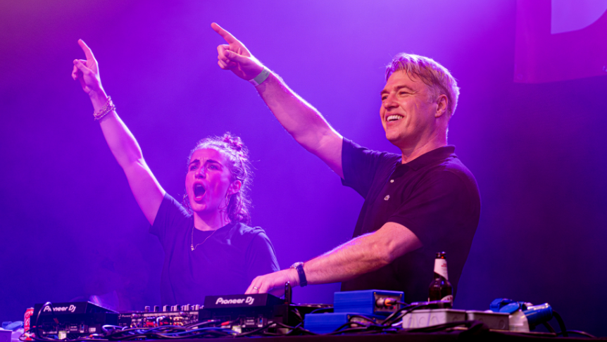 Vicky McClure and Jonny Owen with one arm aloft while standing behind DJ decks