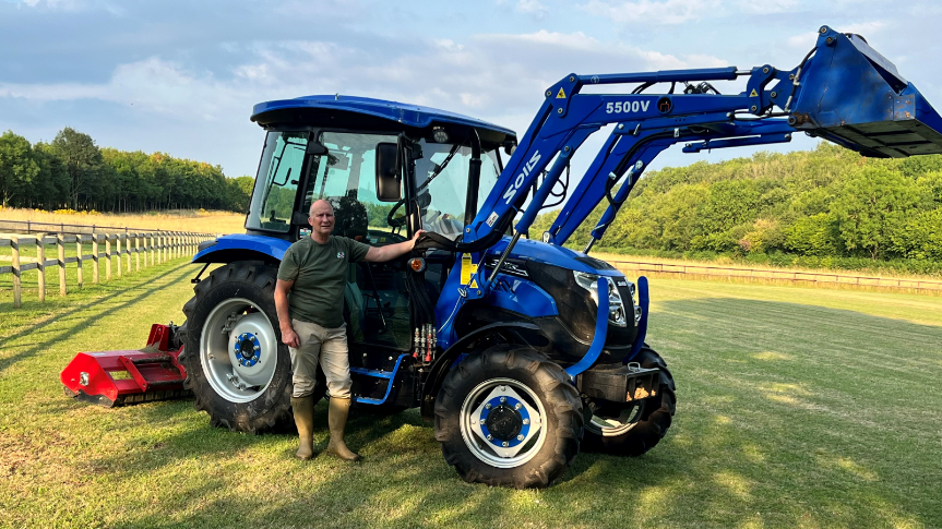 Andrew Gibson standing in front of a blue tractor in a field surrounded by trees