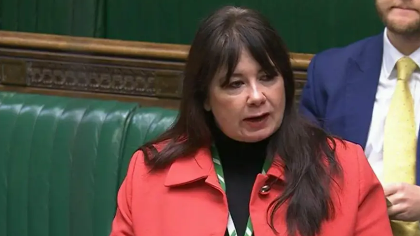 Anneliese Midgley, who has dark hair and is wearing a red jacket, is speaking in the House of Commons.