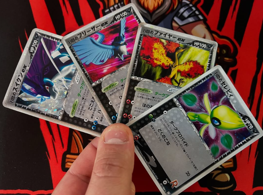 A close-up of four trading cards being held between a person's finger and thumb. The car
