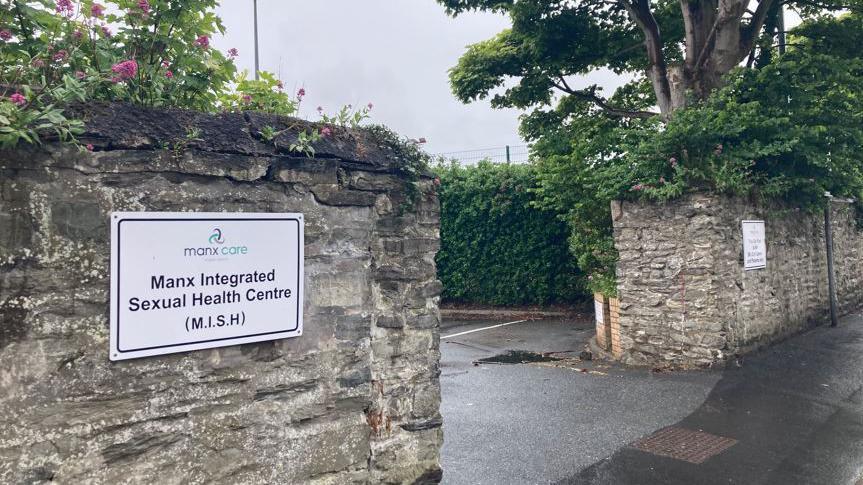 The entrance to the Manx Integrated Sexual Health Centre. The are stone walls either side of the entrance and a white sign on the left.