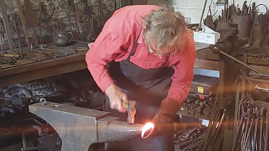 A man hammers on a hot metal ring on an anvil