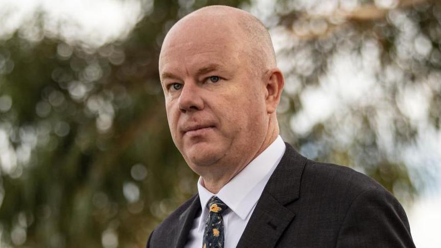 Simon Patterson wearing a suit looks at the camera