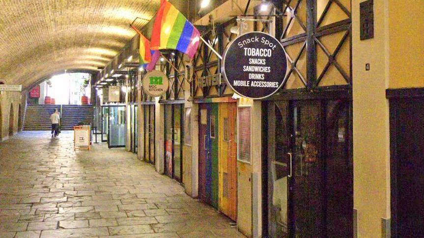 A file image showing the underground arches off Villiers Street, with rainbow doors and Pride flags at the entrance to Heaven visible behind a black round sign for a tobacco shop. Other shop entrances and a staircase can be seen in the background