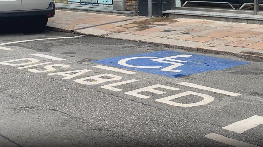 A picture of a blue painted disabled space on a roadside. You can see granite pavement in the background.