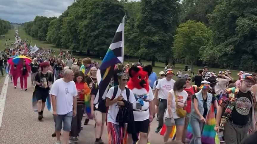 A Pride March along the straight, tree-lined Long Walk at Windsor, with the rows of participants extending back into the distance
