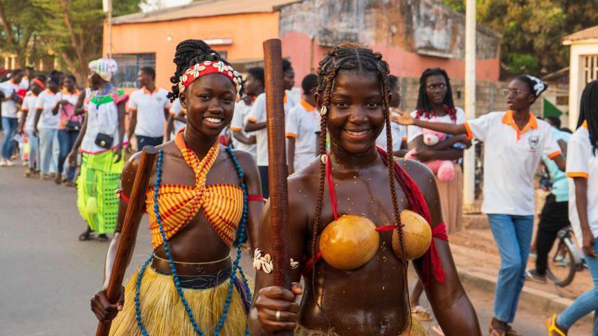 Two members of the Netos de Bandim, a cultural group in Guinea-Bissau, smile at the camera, during the street parade in the capital Bissau - Friday 7 March 2025.