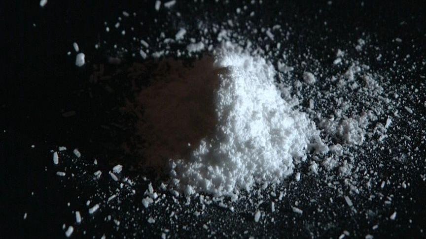 A close-up of a small mound of white powder on a black counter. The right-hand side is illuminated while the left is in shadow.