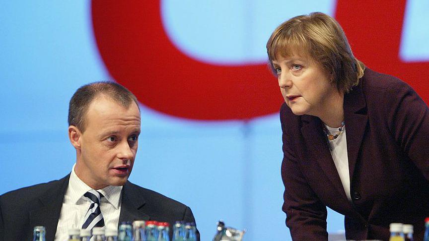 A 2003 image of Merz, sitting down and wearing a striped tie, talking to Angela Merkel