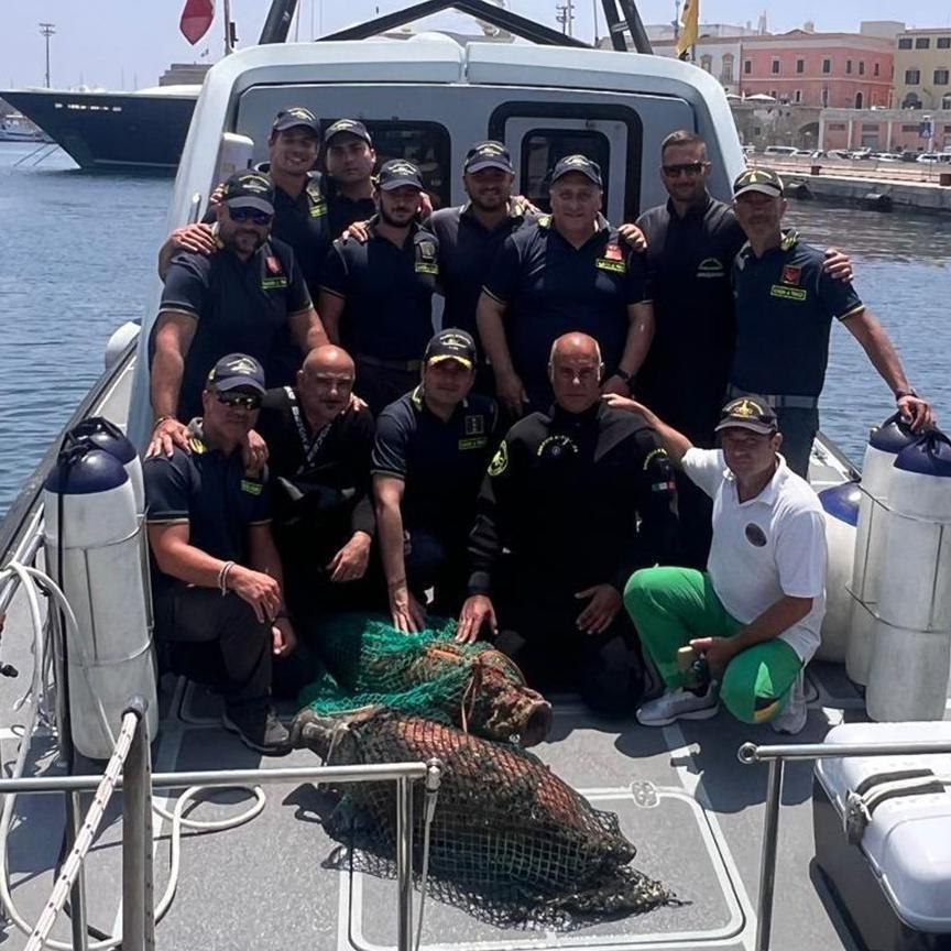A group of divers dress in dark uniforms pose for a photo behind some of the large ceramic jars they excavated from the wreck. 