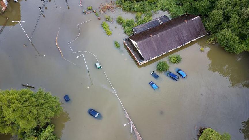 Drone footage of cars and a building in flood water
