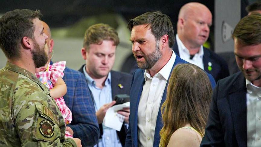 JD Vance, wearing a blue suit and white shirt, surrounded by US soldiers and their families.
