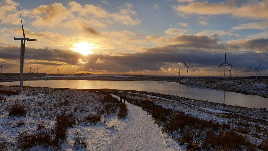 A snowy windfarm borders a reservoir as the sun sets.