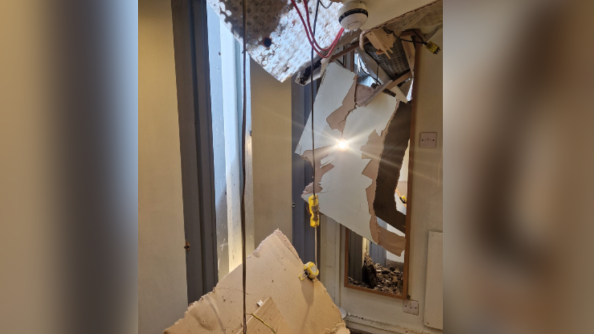 A damaged toilet building, with various bits of roof hanging down