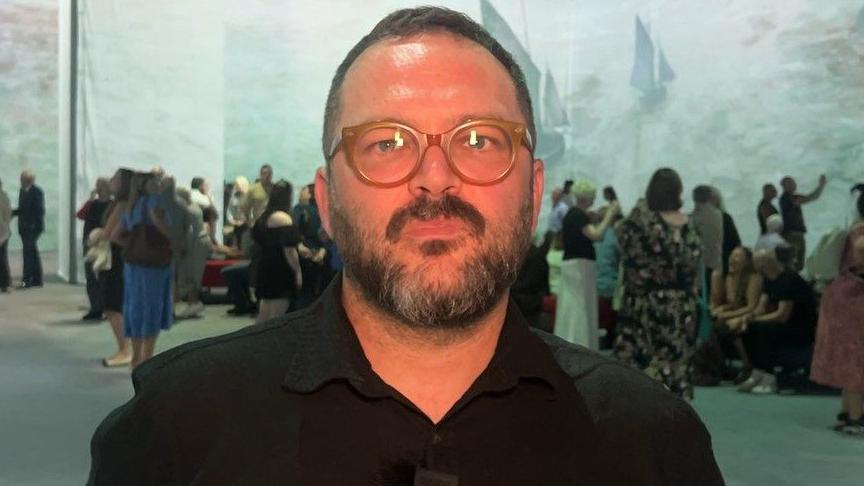 Mathieu St-Arnaud has short receding brown hair with a brown beard specked with grey and large caramel-coloured spectacles.