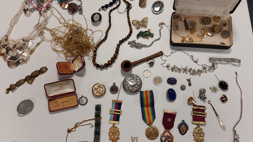 Items of jewellery including brooches and necklaces and a quantity of old coins on a plain white background.