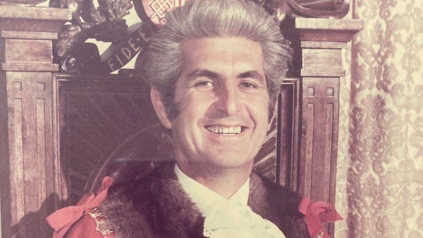 A former mayor wearing his red and black mayoral robes, and the chain of office.
