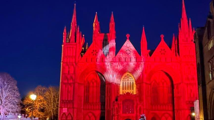 Peterborough Cathedral lit up in red light with a black sky in the background.