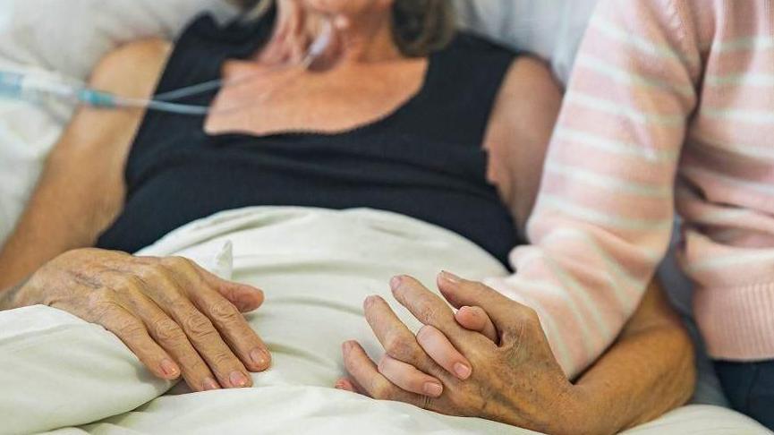 Patient in bed with another person holding their hand