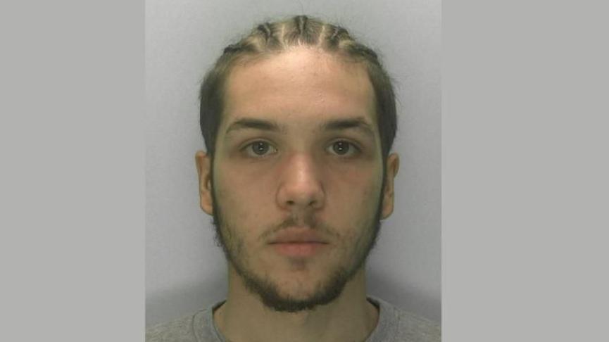 A police mugshot of Kian Westcarr. He has brown hair in braided style on the top of his head and some facial hair