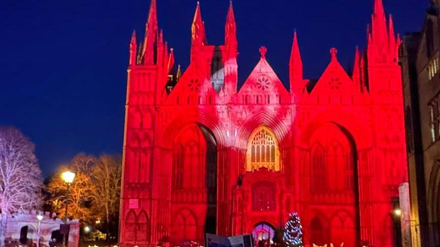 The West Front of Peterborough Cathedral lit up in red at night.