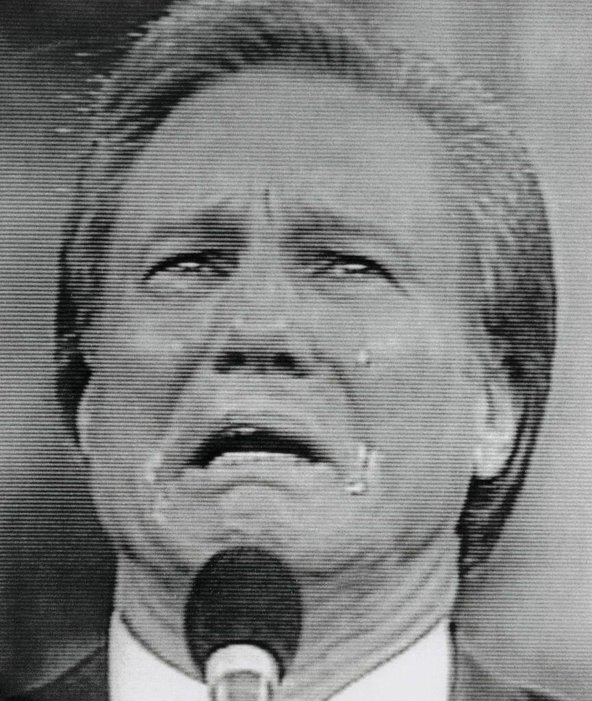 In a black and white screen cap of a 1988 broadcast, Swaggart holds a microphone and weeps