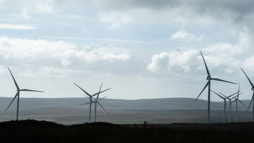 A group of wind turbines in the distance on a hill.
