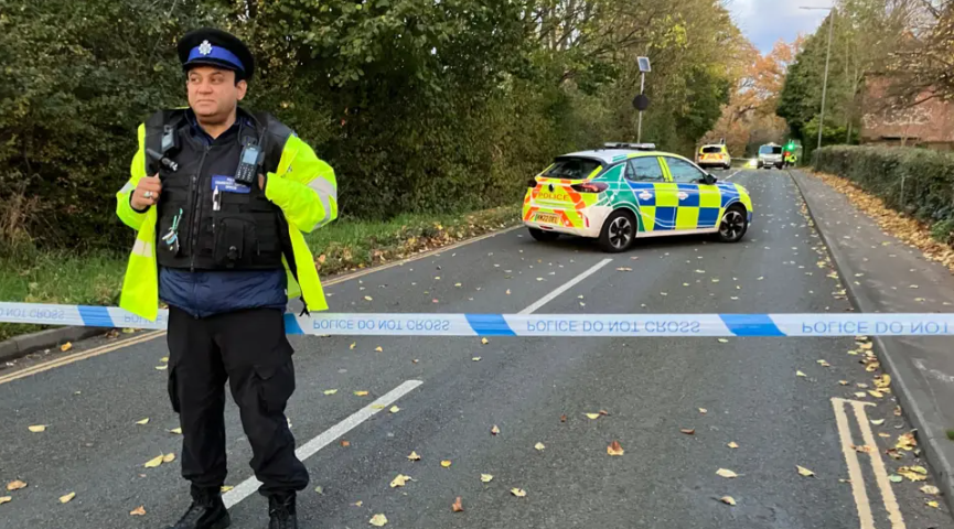 A police officer wearing hi-vis at the cordon to the crash in Lawrence Weston on Sunday. The male police officer is standing in front of police tape. Two police cars are seen within the cordon.