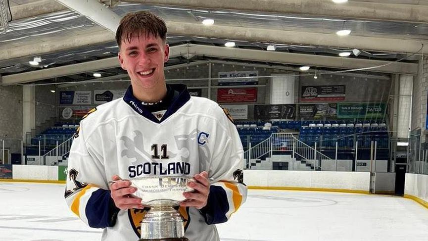 Gary Kelly wears a number 11 Scotland ice hockey shirt and holds the Frank Dempster Trophy